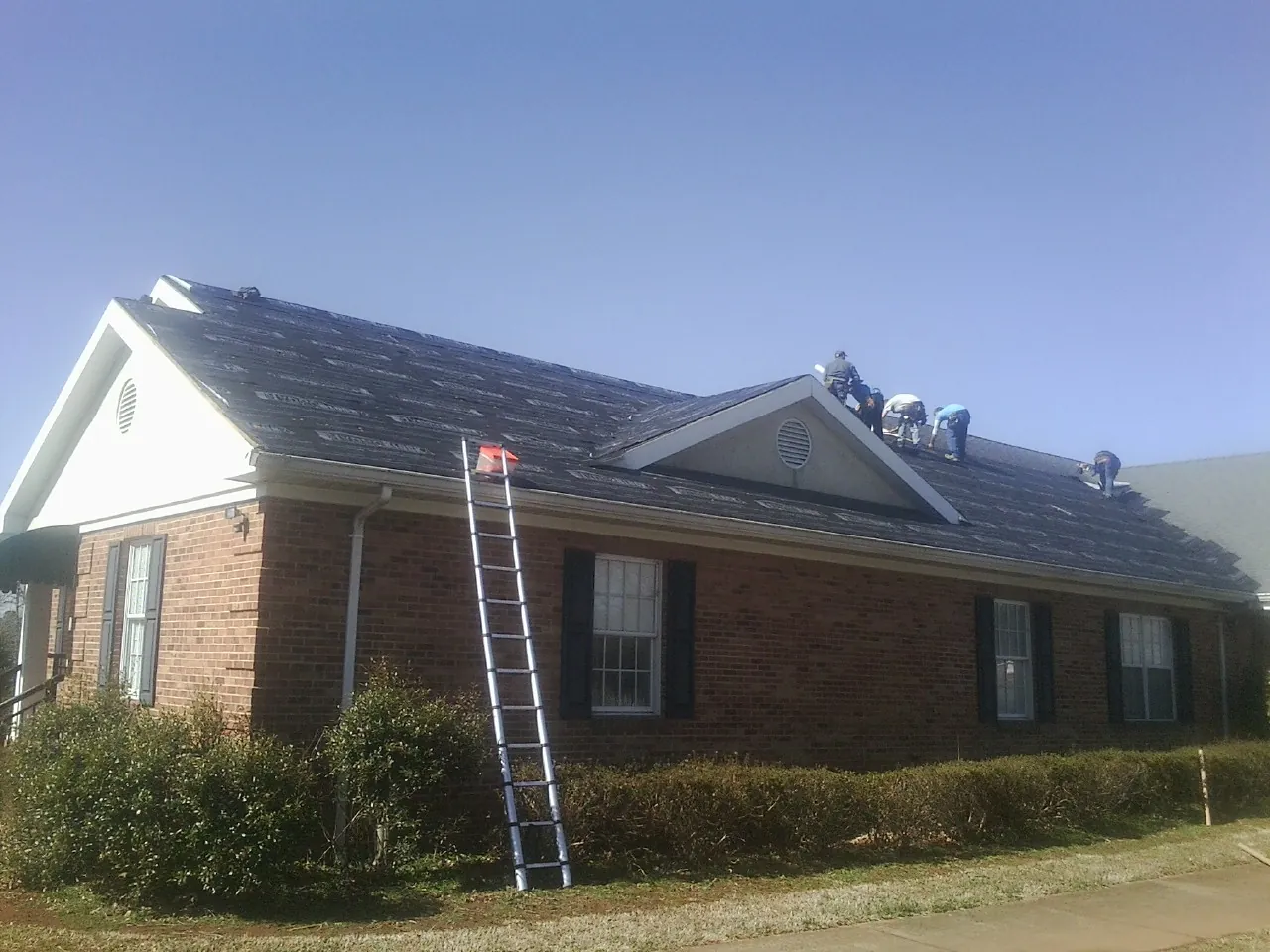 Crew tearing shingles off a brick ranch roof with a ladder set — Metal Roof Repair work by our crew in Shasta