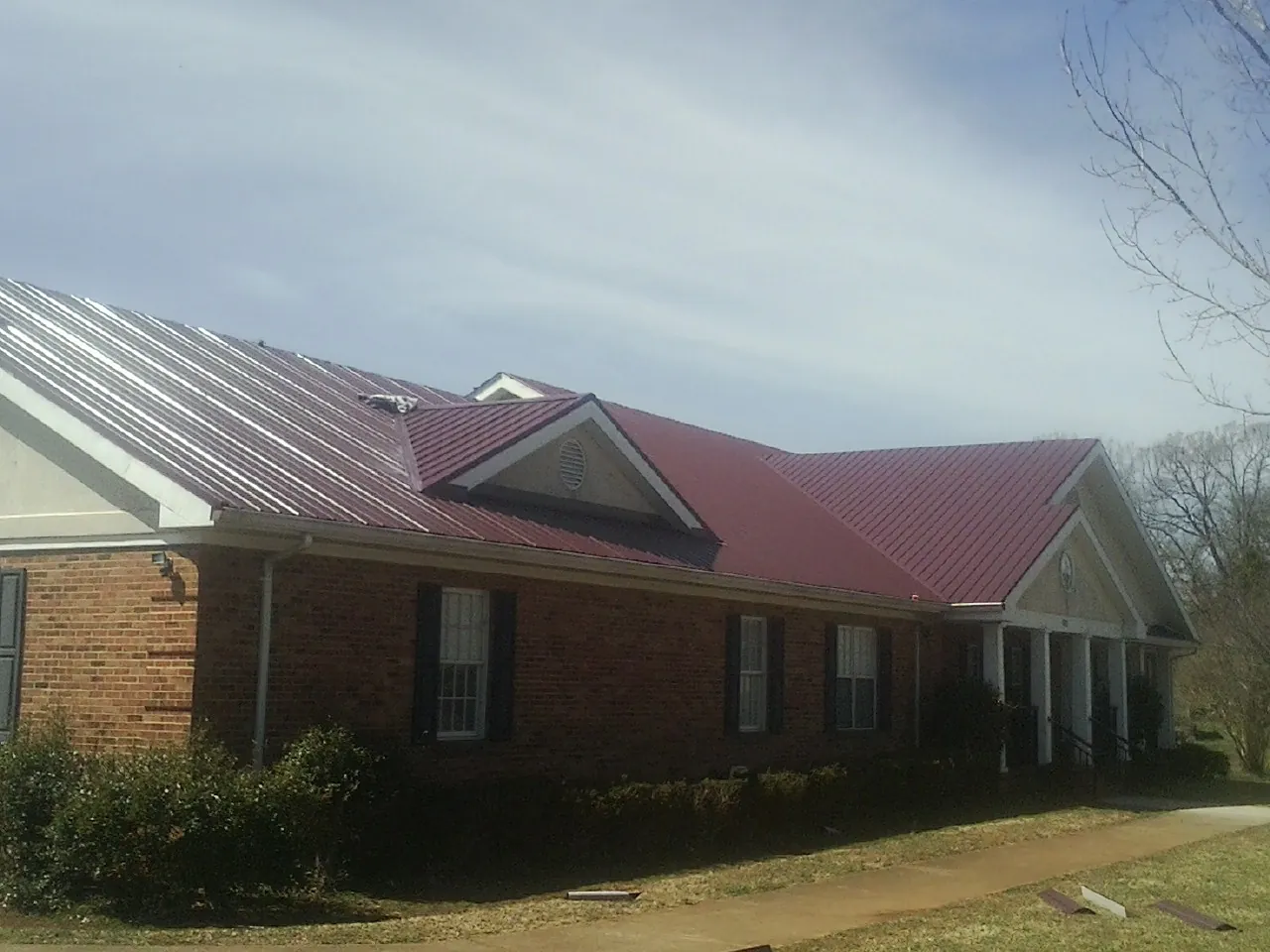 Red metal roof with gabled entries on a long brick building, from a Hail Damage Roof Repair job in Shasta