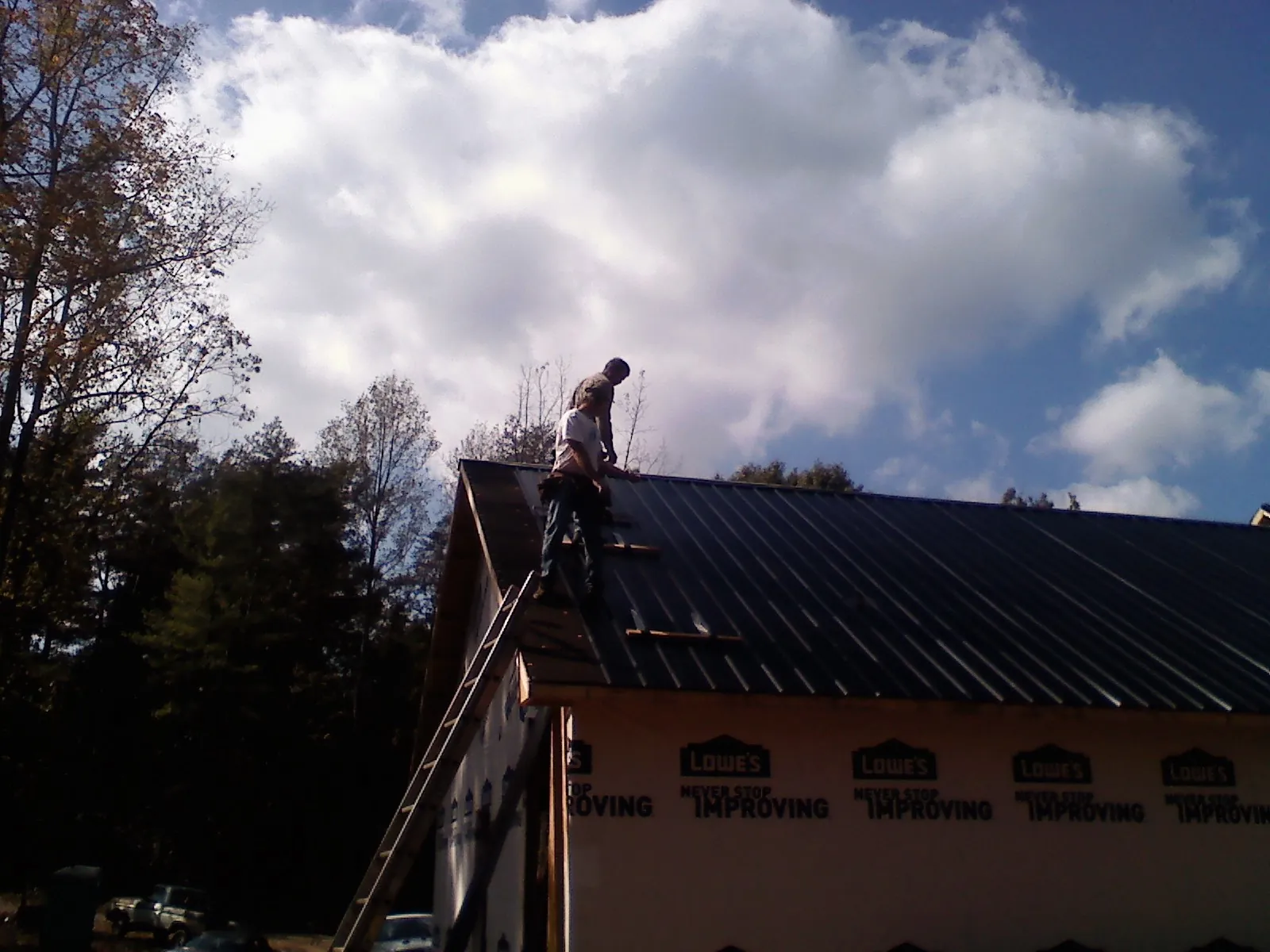 Roofer fastening dark metal panels high against a cloudy sky, from a Roof Inspection job in Shasta