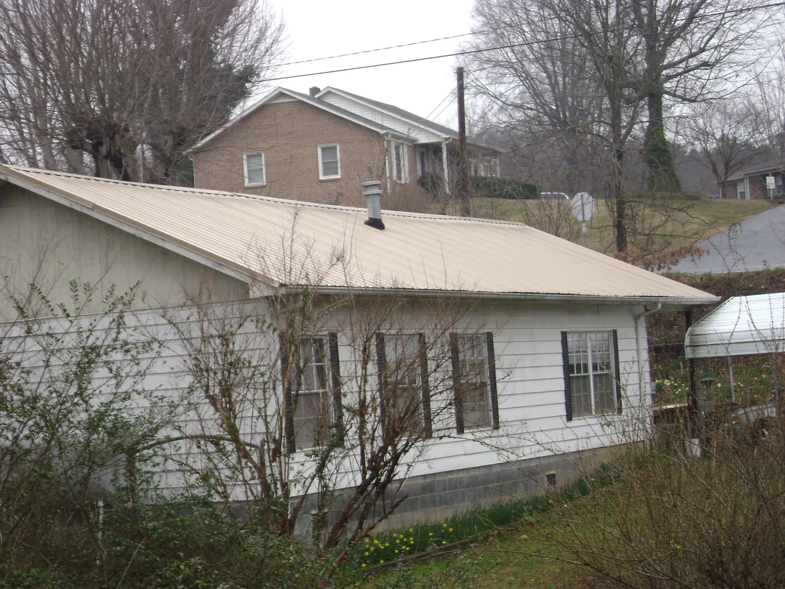 Tan metal roof on a white sided house set into a hillside — Commercial Roofing by Roofing Brothers in Shasta